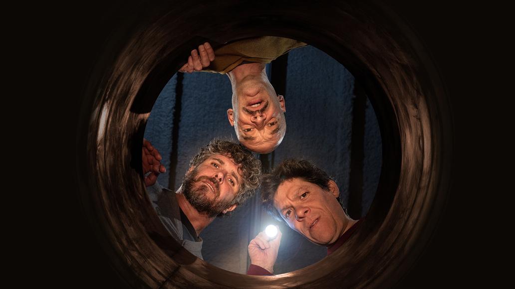 Imatge dels tres actors dels ossos de l'Irlandès. És una imatges zenital (des de baix) on els tres actors treuen el cap per un forat mirant cap abaix.
