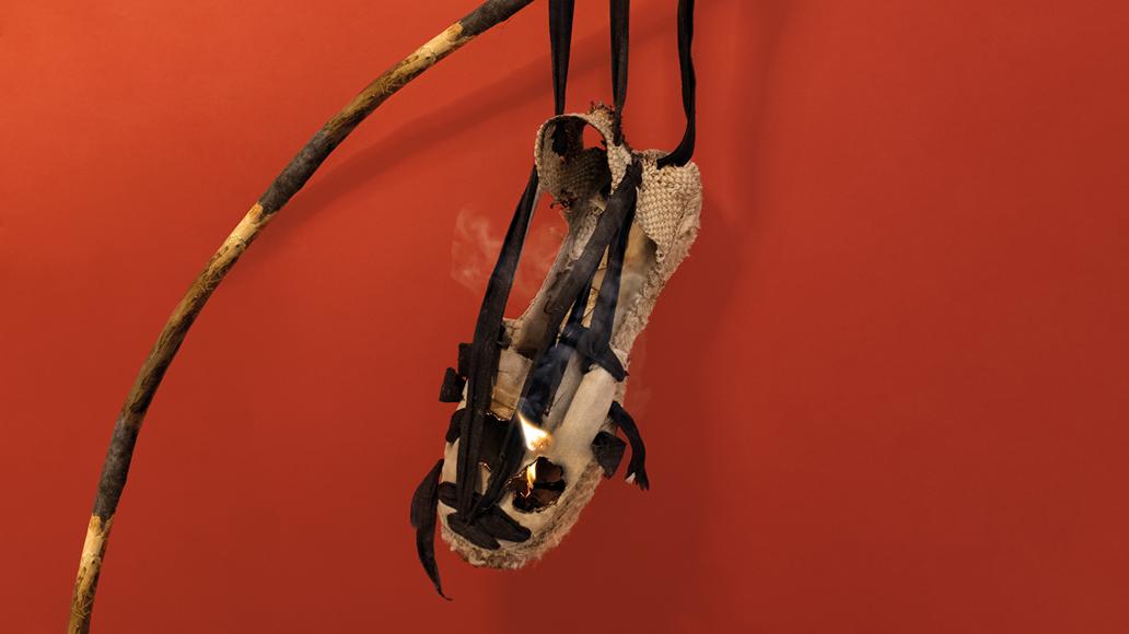 imatge d'una sabata set vetes cremant-se, lligada a una branca d'un arbre amb un fons vermell.